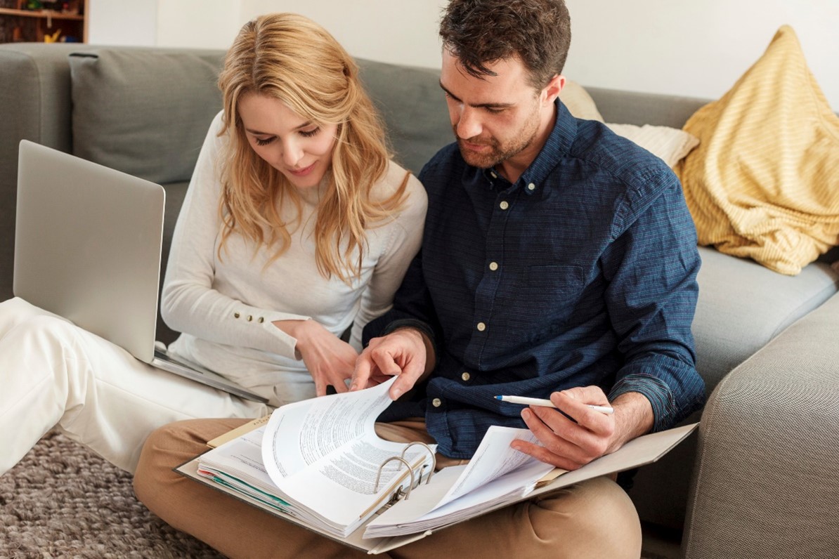 Pariskunta istuu sohvalla ja selaa kansiota täynnä papereita.