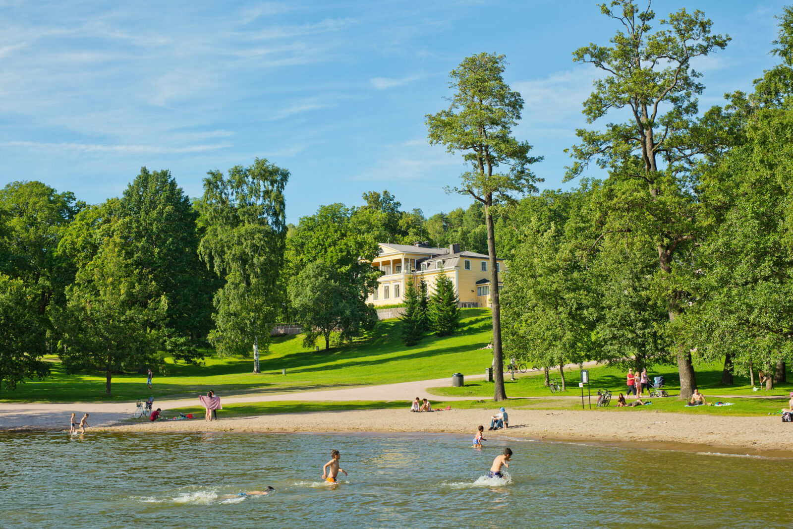 Kuva Mukkulan kartanonpuistosta, jonka rannassa on lapsia uimassa.