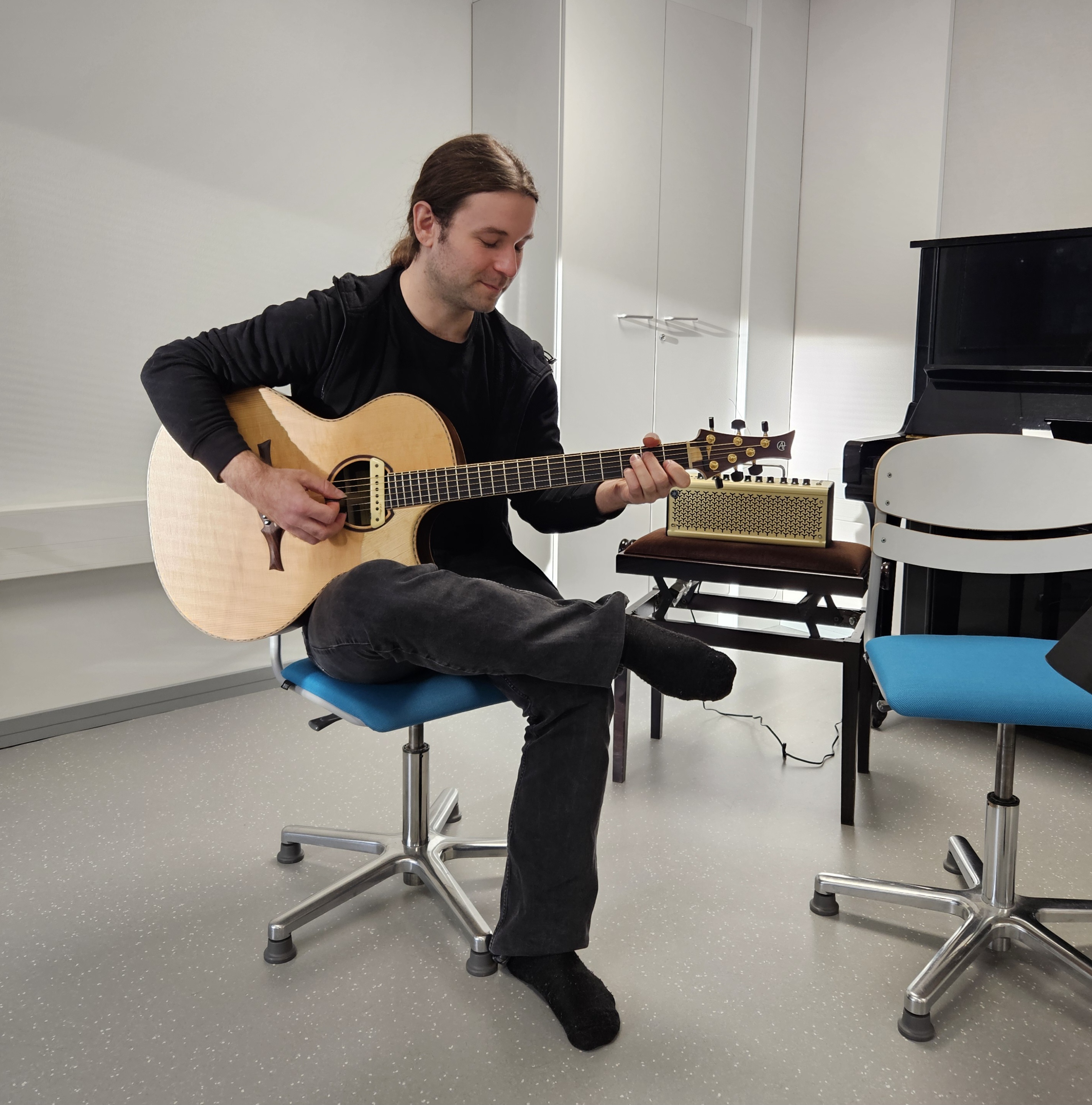 Mies istuu tuolilla ja soittaa kitaraa.